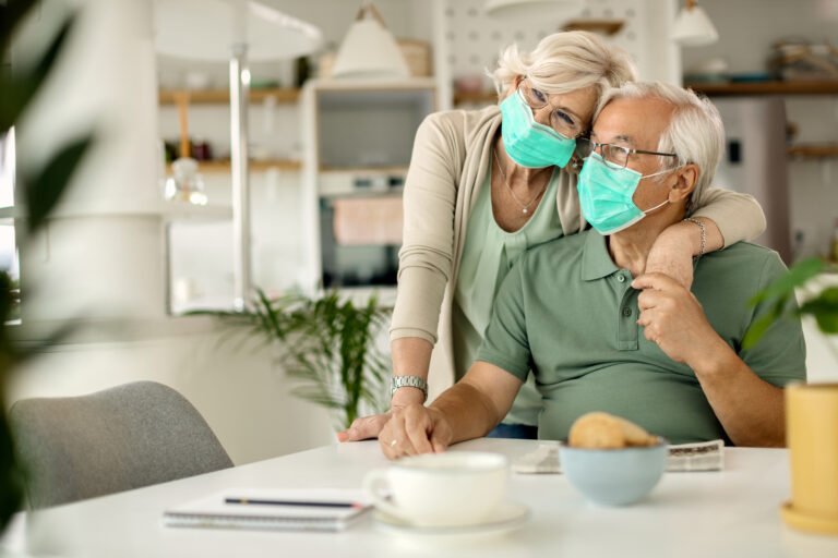 Happy senior couple with protective face masks embracing at home